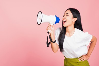 portrait of happy asian beautiful young woman teen confident smiling face holding making announcement message shouting screaming in megaphone, studio shot isolated on pink background, with copy space