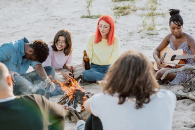 bonfire of friends in open air, outside, dark-skinned beautiful girl plays guitar, rest of people listen, drink beer, joke around, fool around, talk, good atmosphere, time off from school, work