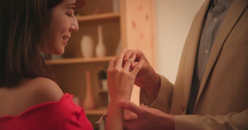 close up of asian man giving propose for marriage to his girlfriend with ring and wear it in living at night home