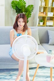 asian happy woman is using mobile phone to turn on electric fan in living room