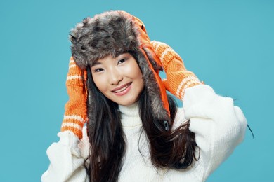 happy woman in gloves holding cap on her head on blue background cropped view