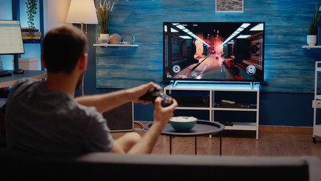 young person playing with modern technology gadget using video games console on television. caucasian gamer with wireless controller sitting at home having fun with digital action