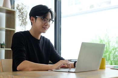 smiling asian man working with laptop computer at home office.