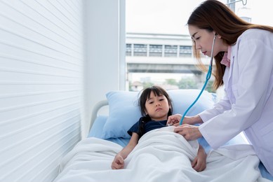 asian woman doctor is using a stethoscope listen to heart rate of a 6 year old patient who came to treat the flu, which is pandemic, to health care and children concept.