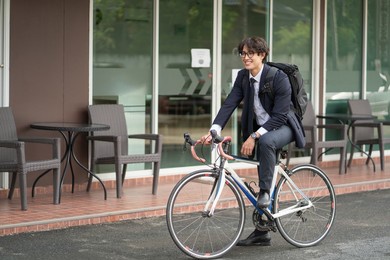 asian businessman in a suit is riding a bicycle on the city streets for his morning commute to work. eco transportation concept	