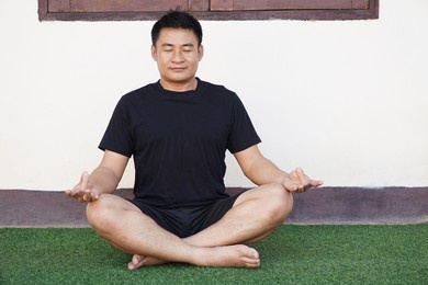 asian middle aged man sits and do meditation in green floor. soft and selective focus.                               