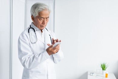 senior asian doctor in white coat using smartphone in hospital