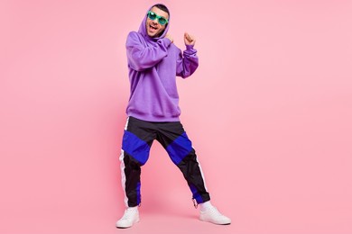 full size photo of funky millennial brunet guy dance wear eyewear hoodie pants shoes isolated on pink background