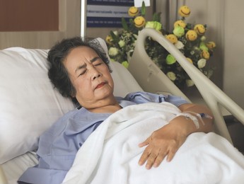 portrait of  lonely asian senior  woman lying in hospital bed, feeling pain. elderly health concept.
