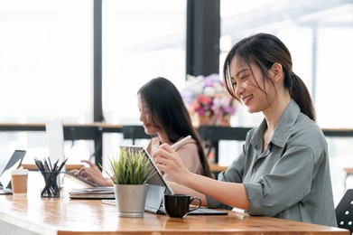 young attractive asian female student using portable tablet with her friend with happiness.