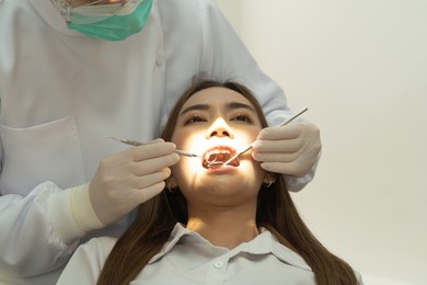 a dentist checking up asian woman patient's teeth by using dental mouth mirror at hospital clinic. teeth check up with dental tools. doctor. dentistry, medical and health. people.