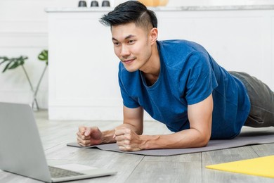 exercises at home concept, asian man practicing yoga at home with laptop with planking on the yoga mats