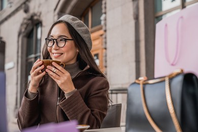 happy asian woman girl student relaxing resting having a coffee tea hot beverage on a street sitting in cafe after shopping outdoors.