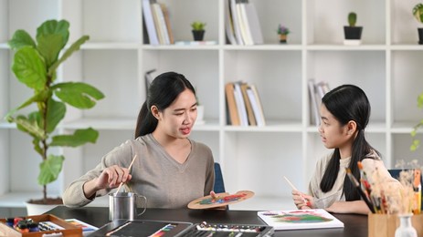 young asian teacher taking care of children while painting pictures in painting course.