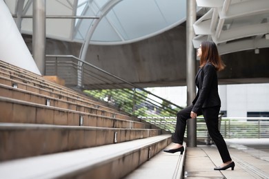 a long-haired woman wearing a mask, suit jacket, trousers and black shoes is walking up the stairs.