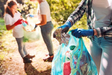 volunteers cleaning up the park, a woman is putting trash in a garbage bag and some kids are helping her, environmental protection concept
