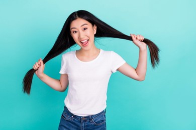 portrait of attractive cheerful long-haired girl making tails having fun isolated over bright teal turquoise color background