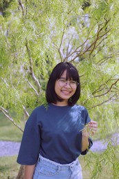 asian teenager toothy smiling and standing under green leaves tree