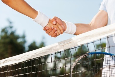 thanking for good game. close-up of man and woman in wristband shaking hands upon the tennis net 