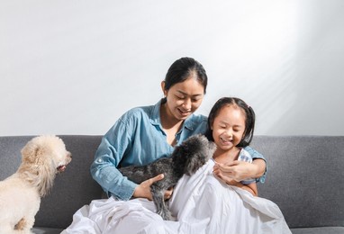 young beautiful mother and little cute daughter have fun playing with dogs on the home sofa. image of happy girl with dog mother relaxing at home. happy family with pet friendship and care concept.