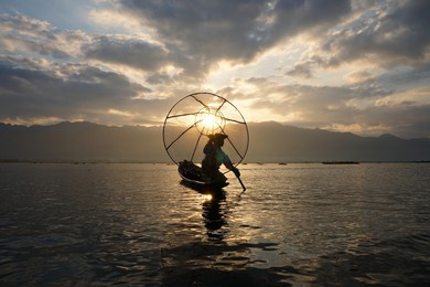 silhouette of local fisherman using coop to catching in inle lake at sunrise