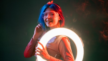 neon light people. futuristic style. modern illumination. cheerful smiling cyberpunk woman with led ring flash lamp in red glow isolated on dark background.