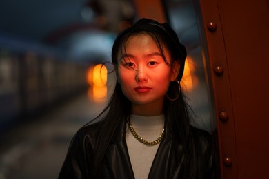fashion street style portrait of young girl of asian ethnicity wear trendy outfit clothes: leather coat, beret and accessories in red neon light. fashionable model, urban style and lifestyle concept