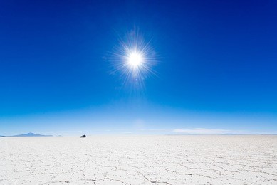 view of the sun over the uyuni salt flats in bolivia with an suv in the background.
