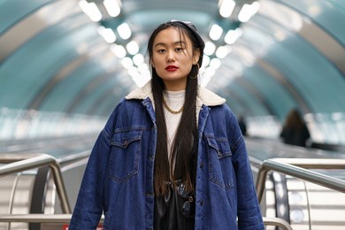 asian girl street fashion portrait: stylish japanese female wearing jeans coat and leather beret on escalator ride to underground station. casual hipster korean woman. urban lifestyle and modern trend