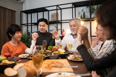 happiness asian multi generation family holding hands and praying on thanksgiving before holiday dinner.thanksgiving celebration tradition asian family dinner concept