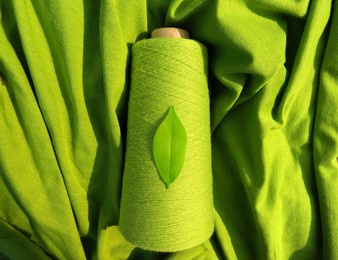 greensustainable fashion:  leaf on a green yarn cone with a backdrop of a green fabric, symbolising sustainability       