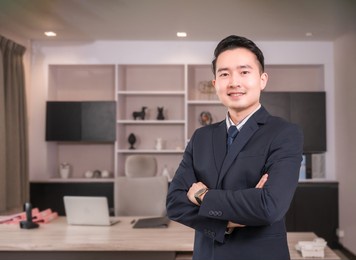 portrait of happy asian businessman ceo in suit with arms crossed and looking at camera in modern room at workplace. handsome male executive financial director standing and smiling success in office.