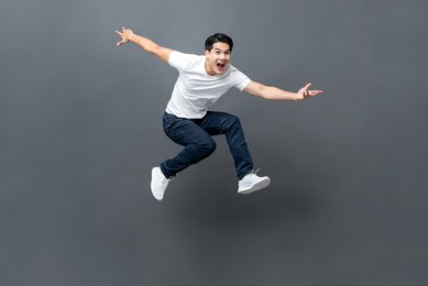 young handsome energetic asian man jumping with hands outstratched in isolated studio gray background