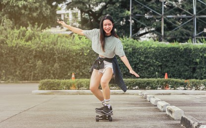 beautiful happy asian healthy woman smiling, holding sweet lollipop, riding and playing extreme sportive skateboard as outdoor activity with happiness, relaxation during holidays in summer vacation