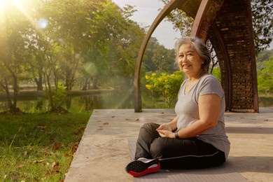 healthy gray-haired asian elderly woman meditates on the siemens floor in a park during a yoga session in the warm morning sun : retirement health care and life insurance.