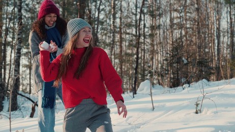 two happy excited multiethnic young women fight snowballs with friends in beautiful sunny snowy forest slow motion.