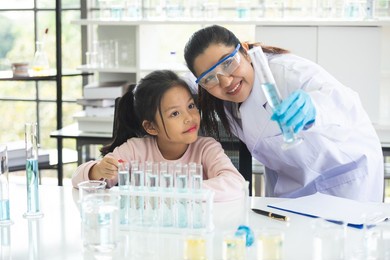 little asian children girl in elementary science class doing chemical experiment helped by woman teacher test, experimen, try drop color water to plate. education science workshop concept.