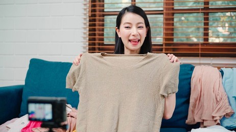 asian stylist fashion influencer designer women using camera streaming and live to sell clothes, product, and accessories business, e-commerce broadcast online on sofa in living room at home.