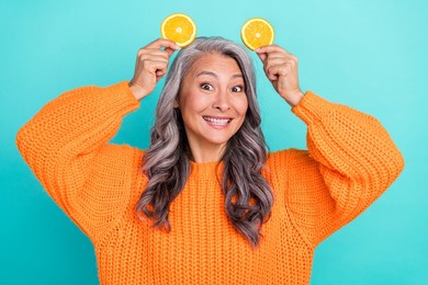 photo of mature lovely woman have fun hold orange pieces like pet ears isolated over teal color background