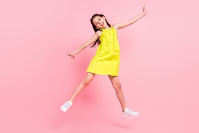 full length photo of sweet shiny school girl wear yellow dress dark eyewear jumping high isolated pink color background