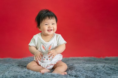 asian happy baby smiling and sitting on red color background. cute 6 months baby with copy space use as concept of bedroom, drypers, development, baby or kid department in hospital.