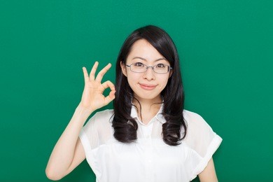 young business woman with glasses showing ok gesture, against green background 
