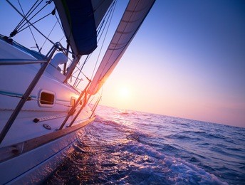 sail boat gliding in open sea at sunset