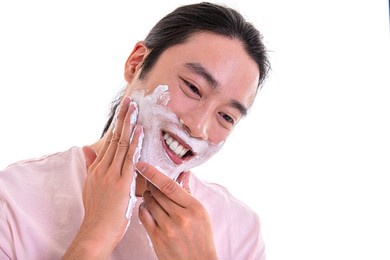 asian man applying shaving foam on his face with his hands. isolated on white background