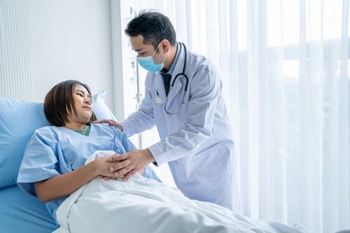asian male doctor caring for a female patient who is lying in hospital