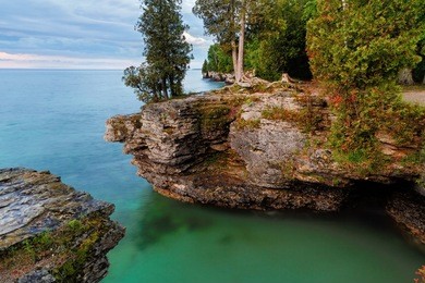 early morning long exposure photo at door county, wisconsin's cave point, on lake michigan, reveals rocky cliffs, colorful waters, and a cloudy sky.