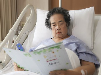 portrait of  asian senior female patient  sitting and reading food menu in hospital bed, ordering food. elderly health concept.