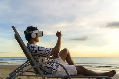 young asian man using virtual reality glasses for business meeting on the tropical beach over beautiful sea and sky background