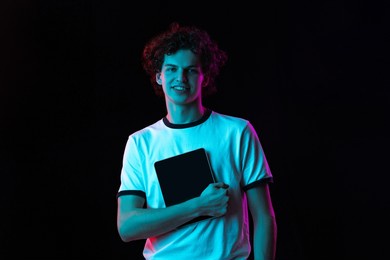 online education. portrait of young man in white t-shirt with tablet isolated over black background in neon lights concept of feelings, youth, fashion, facial expression, emotions, lifestyle, ad