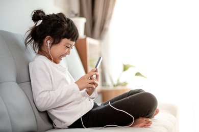 pretty asian girl using headphones for listen to music by smartphone in living room